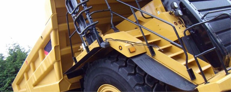 Gelber Bagger mit großen Rädern und Sicherheitsgeländern auf einer Baustelle.