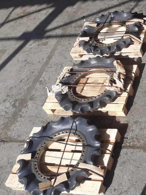 Three khaki-colored mantis tread components on wooden pallets outdoors.